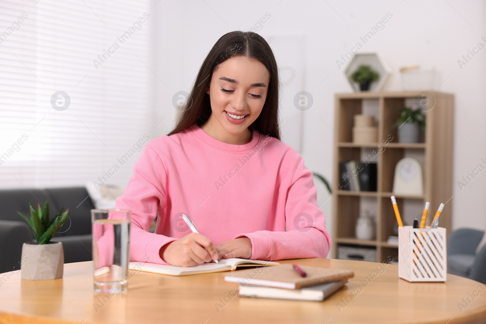 Photo of Young woman writing in notebook at wooden table indoors