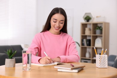 Young woman writing in notebook at wooden table indoors