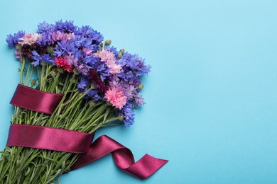 Photo of Bouquet of beautiful cornflowers on light blue background, top view. Space for text
