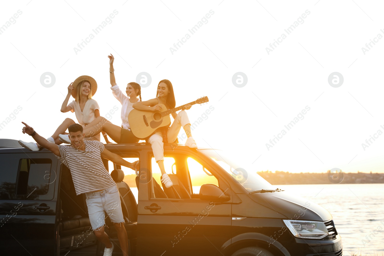 Photo of Happy friends with guitar near sea at sunset. Summer trip