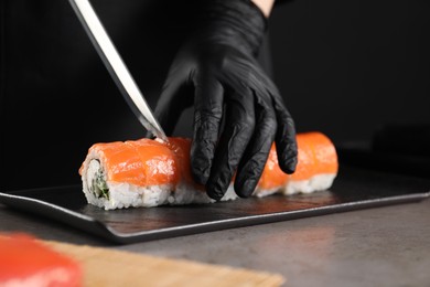 Chef in gloves cutting sushi roll at grey table, closeup