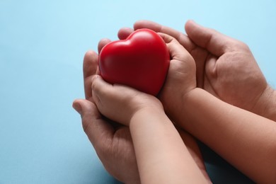 Father and his child holding red decorative heart on light blue background, closeup