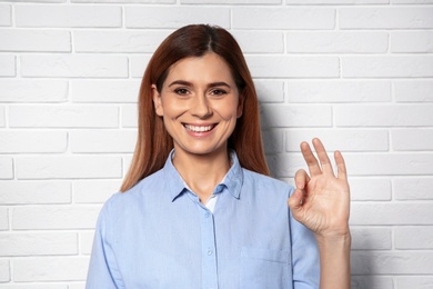 Photo of Woman showing OK gesture in sign language near brick wall
