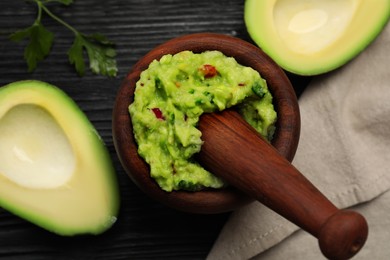 Mortar with delicious guacamole and ingredients on black wooden table, flat lay