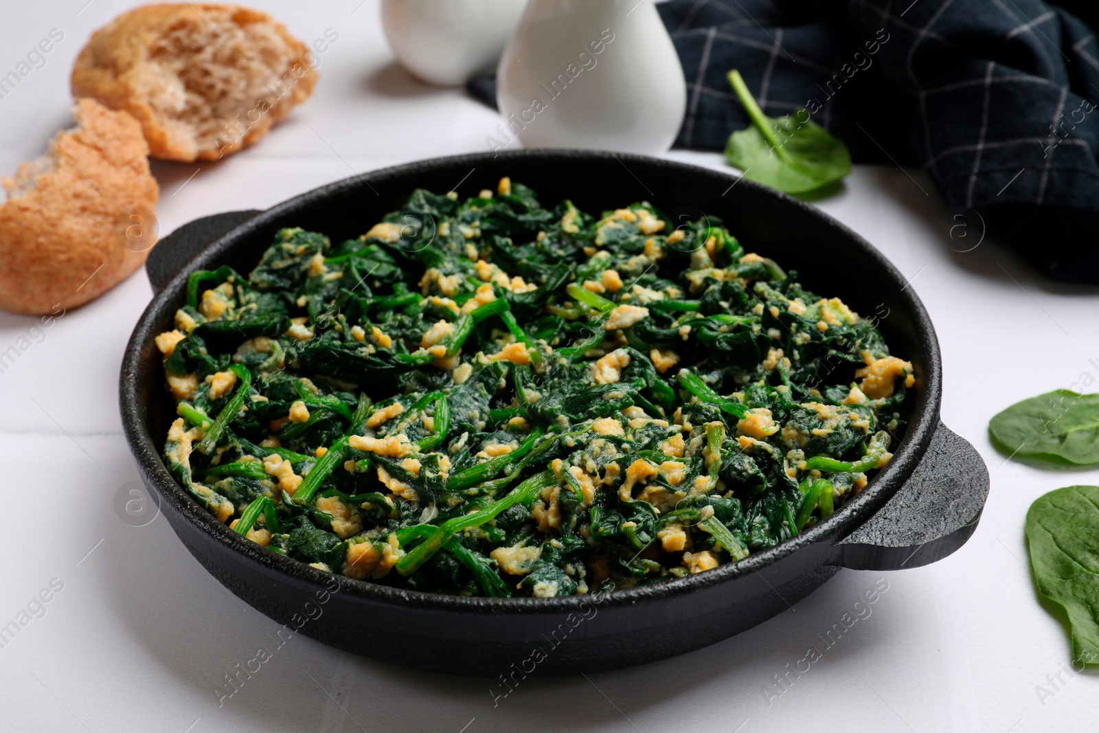 Photo of Tasty spinach dip with eggs in dish served on white tiled table, closeup