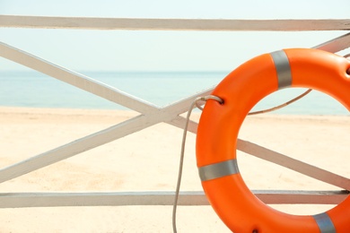 Photo of Orange life buoy near wooden railing on beach, closeup.  Emergency rescue equipment