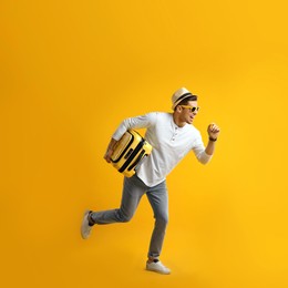 Male tourist with suitcase running on yellow background