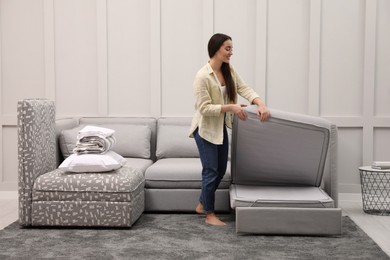 Photo of Woman making sleeping place for guest in living room. Convertible sofa