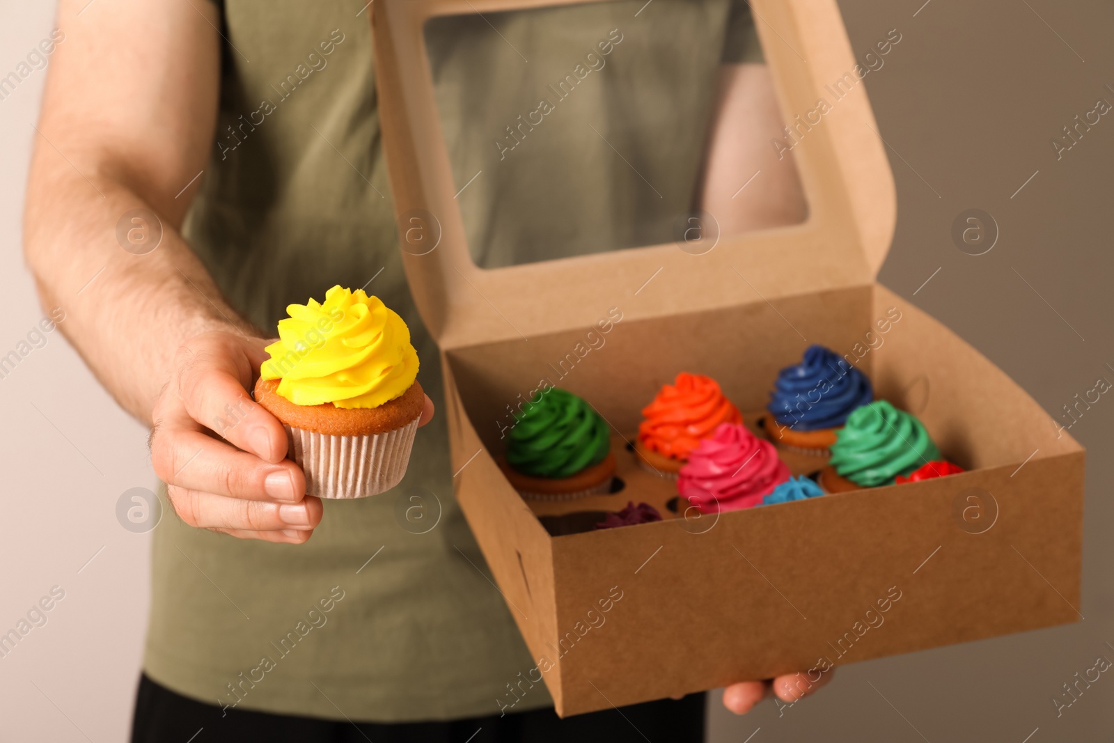 Photo of Man holding box with delicious colorful cupcakes on grey background, closeup
