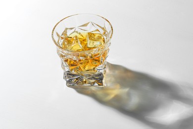 Whiskey with ice cubes in glass on white table