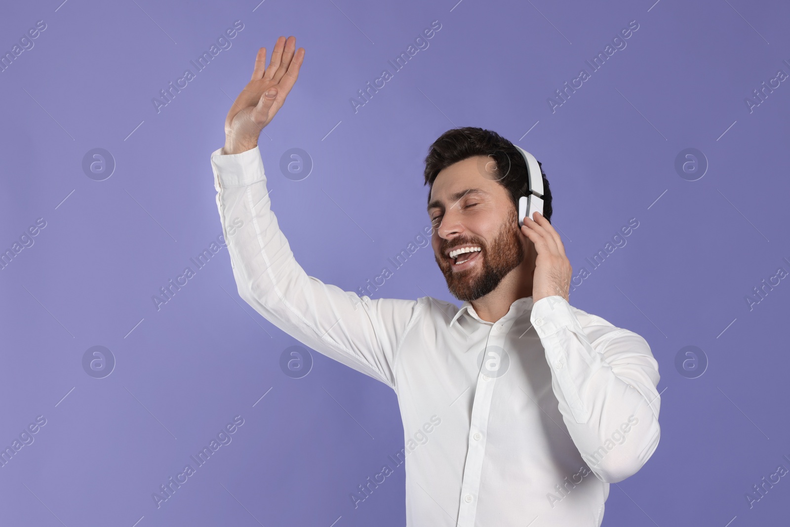 Photo of Happy man listening music with headphones on violet background. Space for text