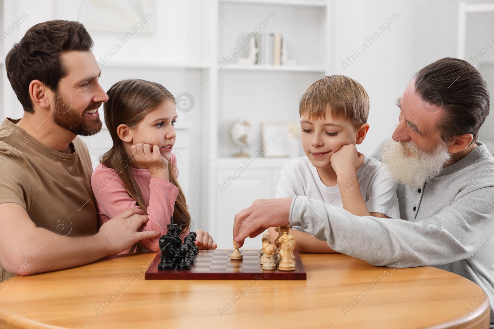 Photo of Family playing chess together at table in room