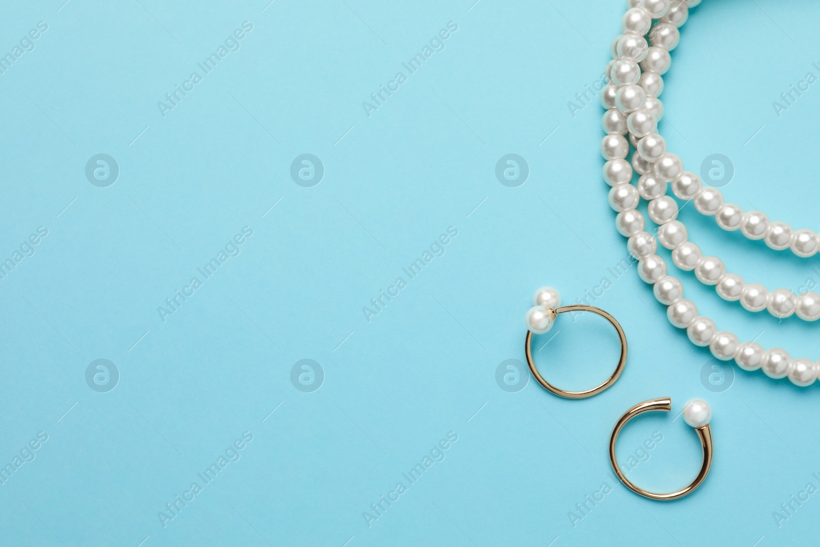 Photo of Elegant necklace and golden rings with pearls on light blue background, flat lay. Space for text