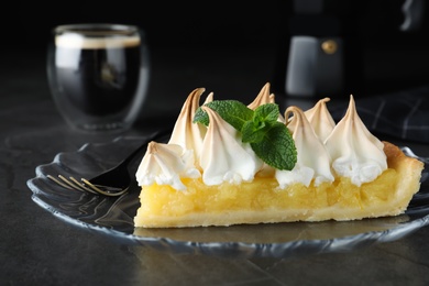 Photo of Piece of delicious lemon meringue pie with mint served on black table, closeup