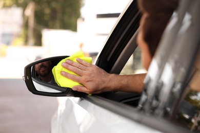 Photo of Smiling man cleaning car side mirror with rag, view from outside