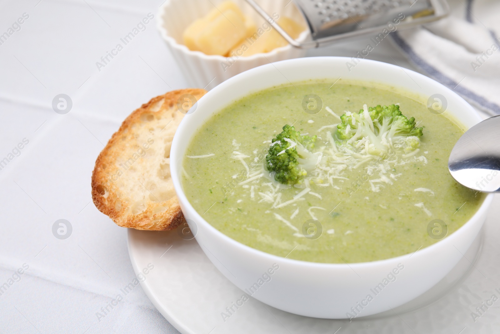 Photo of Delicious broccoli cream soup with cheese served on white tiled table, closeup. Space for text