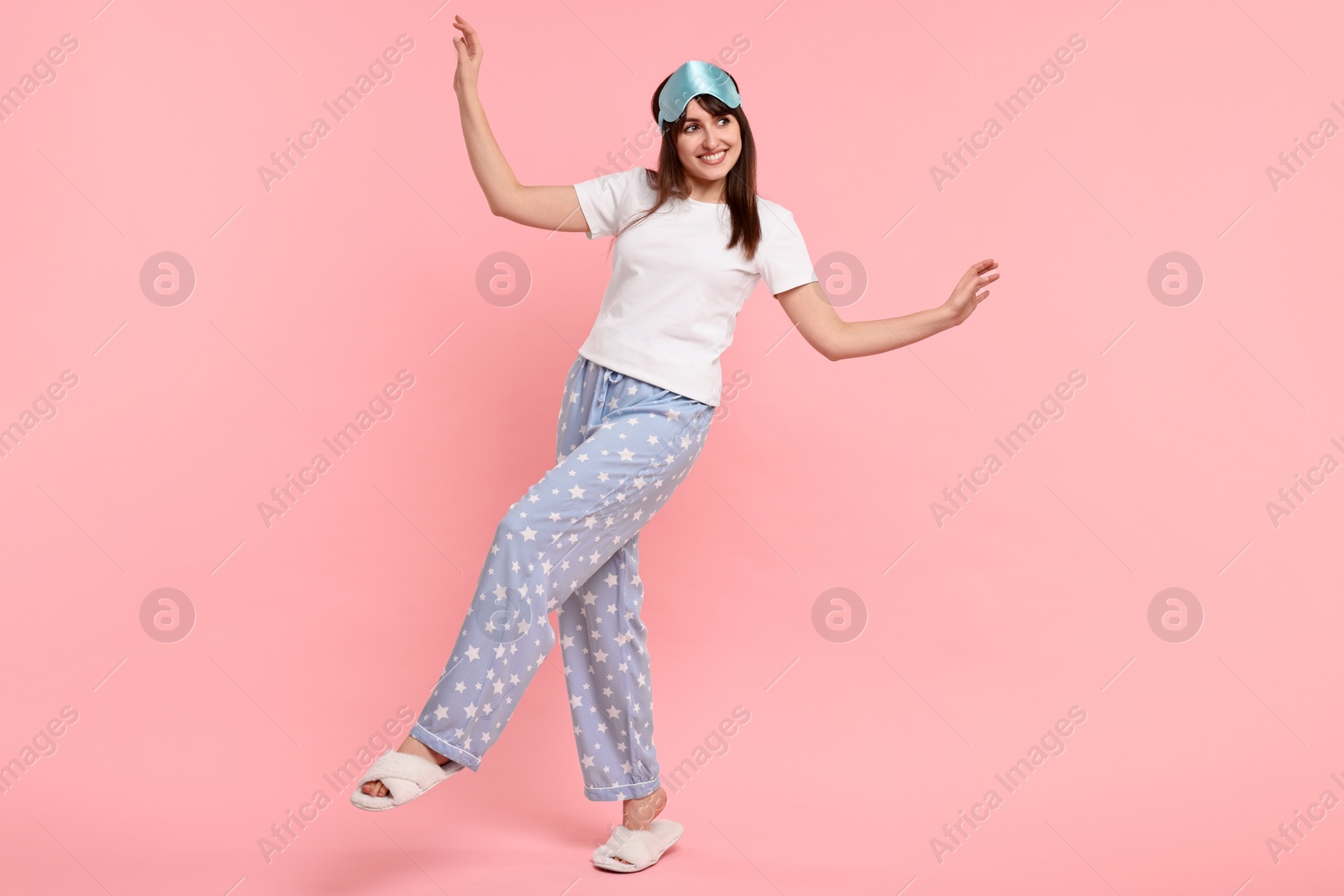 Photo of Happy woman in pyjama and sleep mask on pink background