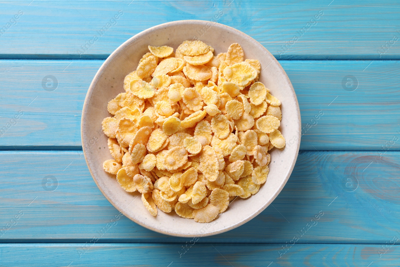 Photo of Bowl of tasty crispy corn flakes on light blue wooden table, top view