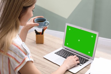 Young woman using laptop at wooden desk. Device display with chroma key