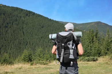 Man with backpack and sleeping mat in mountains, back view. Space for text