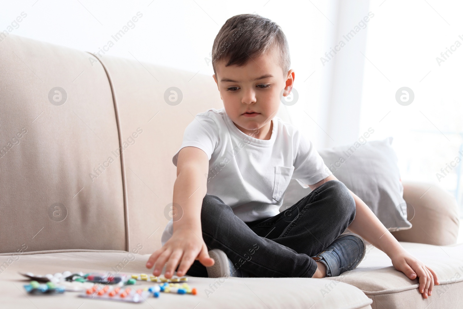 Photo of Little child with different pills on sofa at home. Household danger