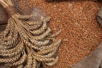 Sack with wheat grains and spikelets on wooden table, top view