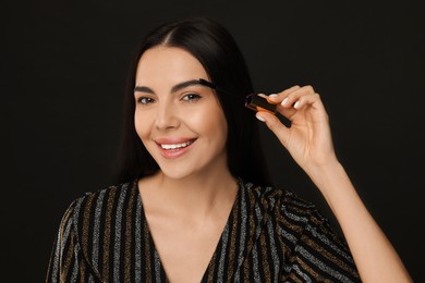 Photo of Beautiful young woman applying mascara on black background