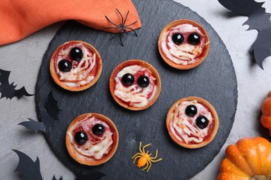 Photo of Cute monster tartlets served on grey table, flat lay. Halloween party food