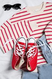 Photo of Pair of stylish red shoes, clothes and sunglasses on white fabric, flat lay