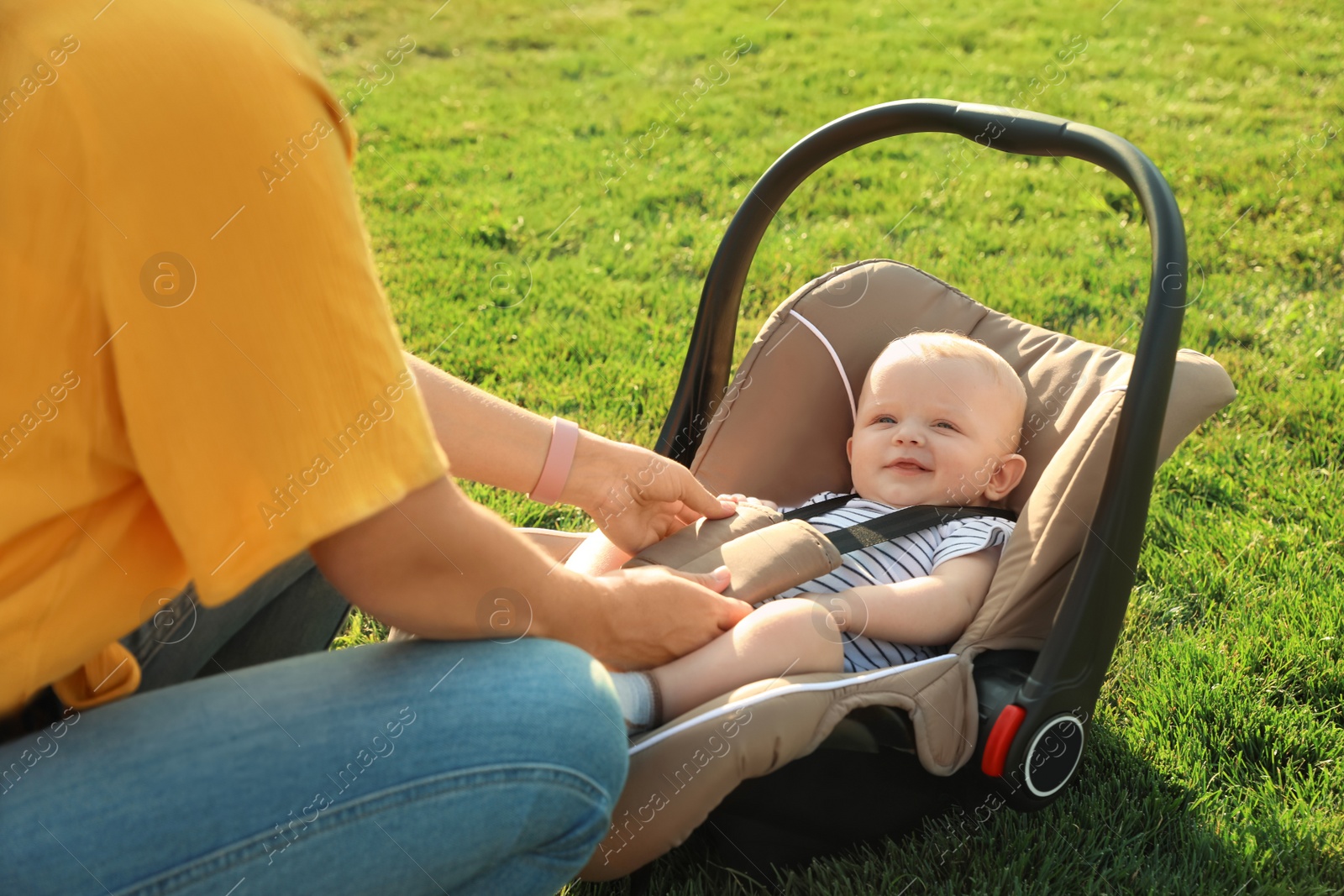 Photo of Mother fastening baby to child safety seat outdoors