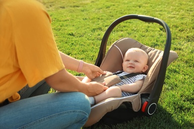 Mother fastening baby to child safety seat outdoors