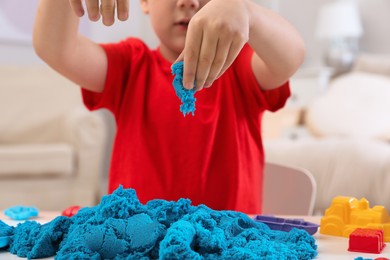 Photo of Little boy playing with bright kinetic sand at table indoors, closeup