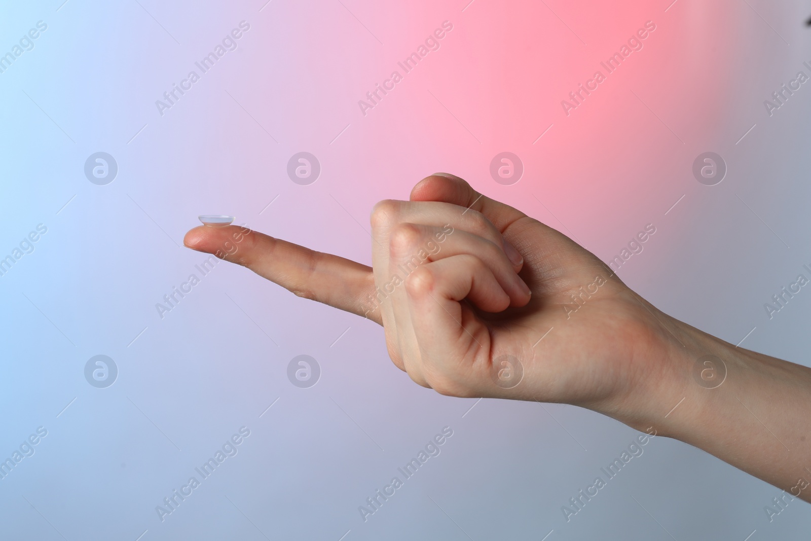 Photo of Woman holding contact lens on color background, closeup