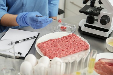 Photo of Scientist checking meat at table in laboratory, closeup. Quality control