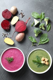 Tasty cream soups in bowls and ingredients on dark grey table, flat lay