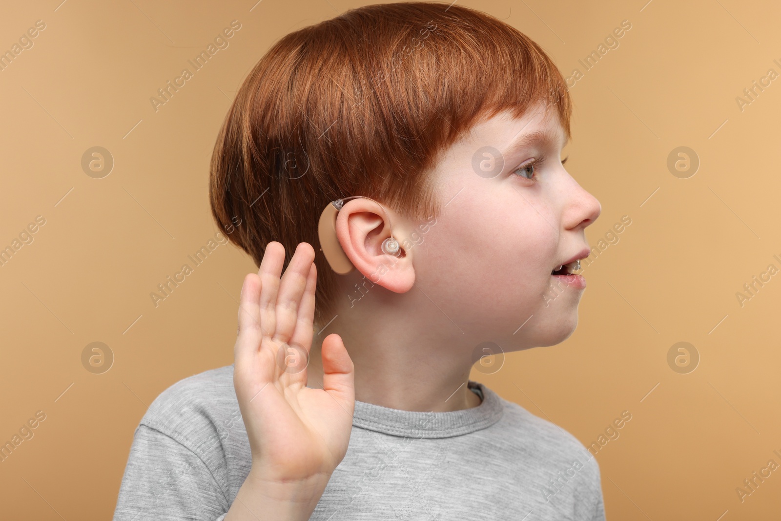 Photo of Little boy with hearing aid on pale brown background