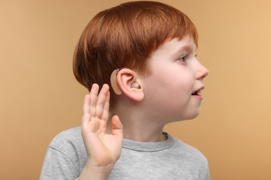 Little boy with hearing aid on pale brown background