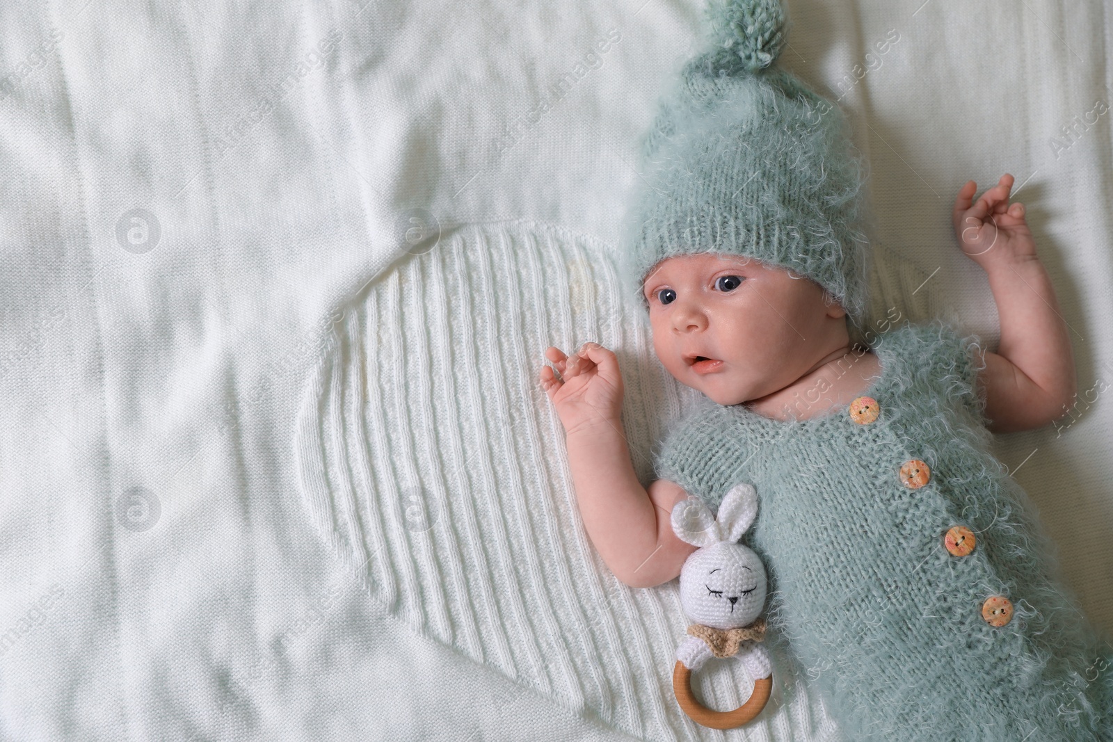 Photo of Cute newborn baby with teething toy on white blanket, top view. Space for text