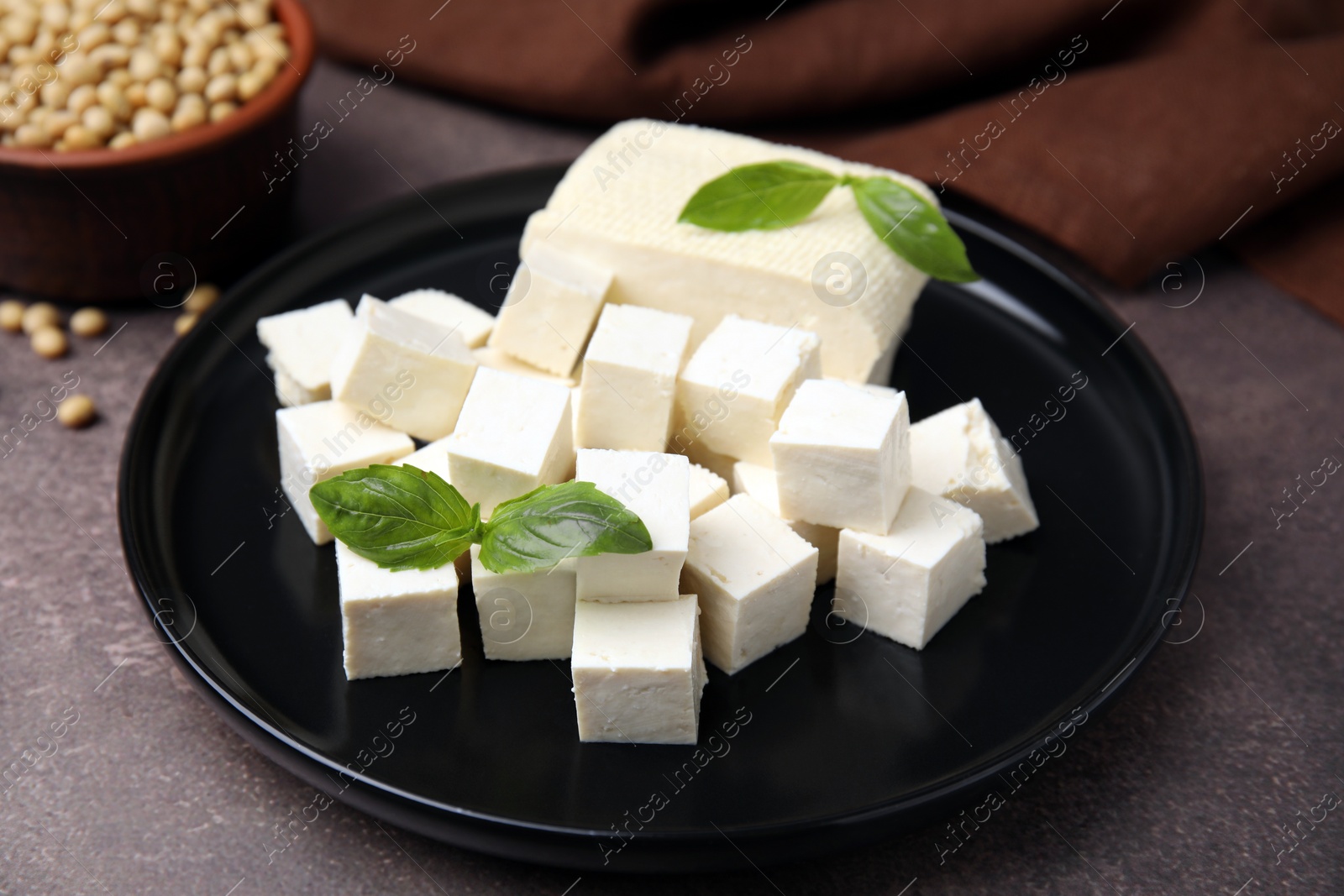 Photo of Delicious tofu cheese, basil and soybeans on brown textured table, closeup