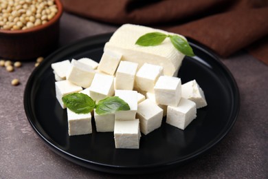 Delicious tofu cheese, basil and soybeans on brown textured table, closeup