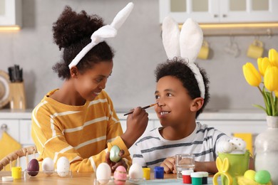 Happy African American mother and her cute son having fun while painting Easter eggs at table in kitchen
