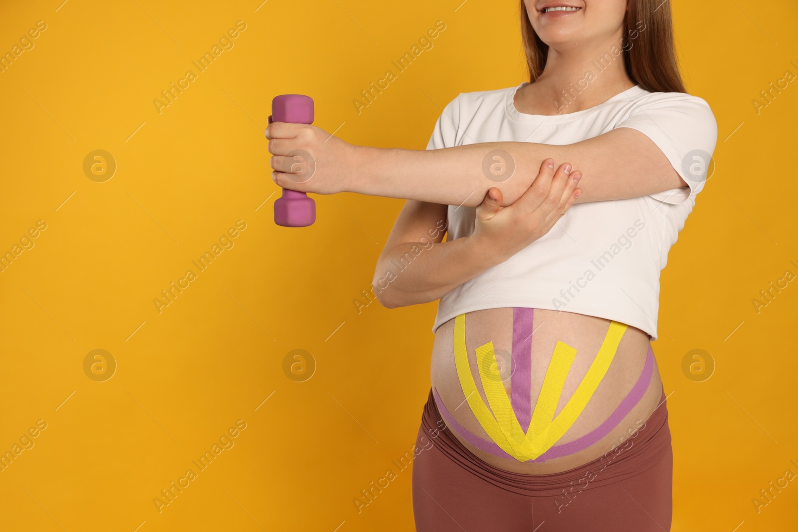 Photo of Pregnant woman with kinesio tapes on her belly doing exercises against orange background, closeup. Space for text