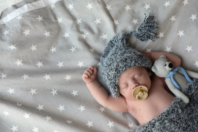 Photo of Cute newborn baby in warm hat with toy sleeping on bed, top view. Space for text