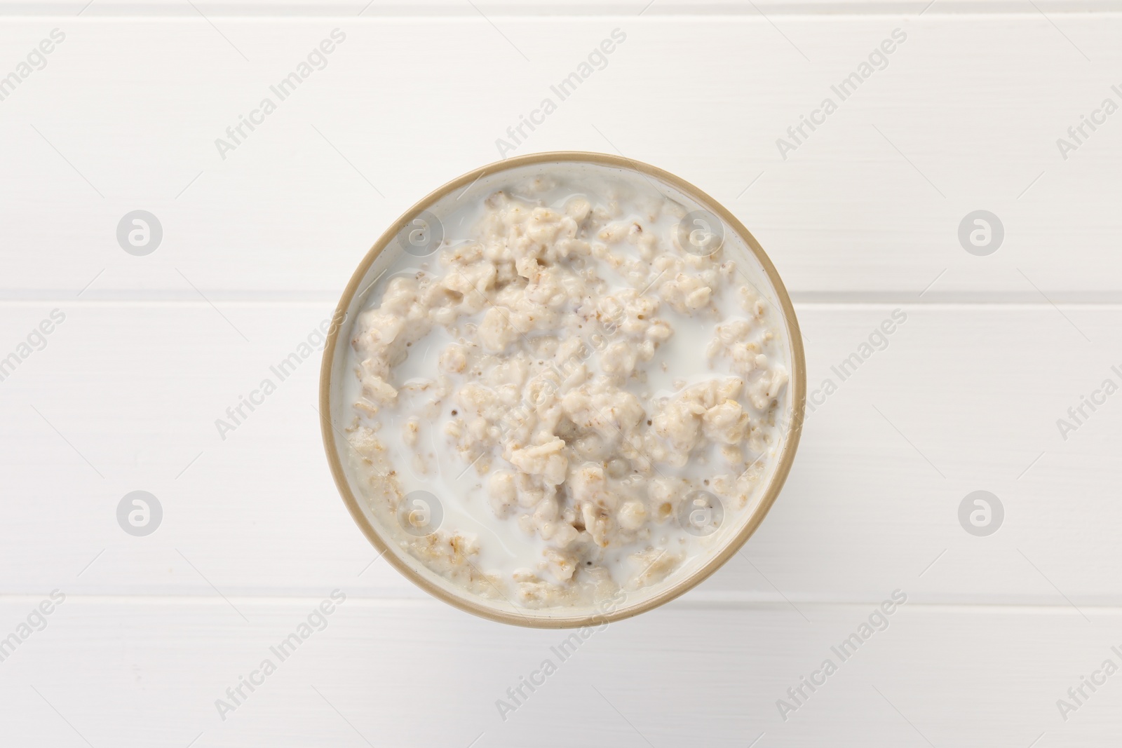 Photo of Tasty boiled oatmeal in bowl on white wooden table, top view