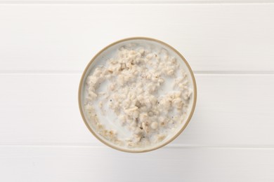 Photo of Tasty boiled oatmeal in bowl on white wooden table, top view