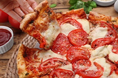 Woman taking piece of delicious Caprese pizza at wooden table, closeup