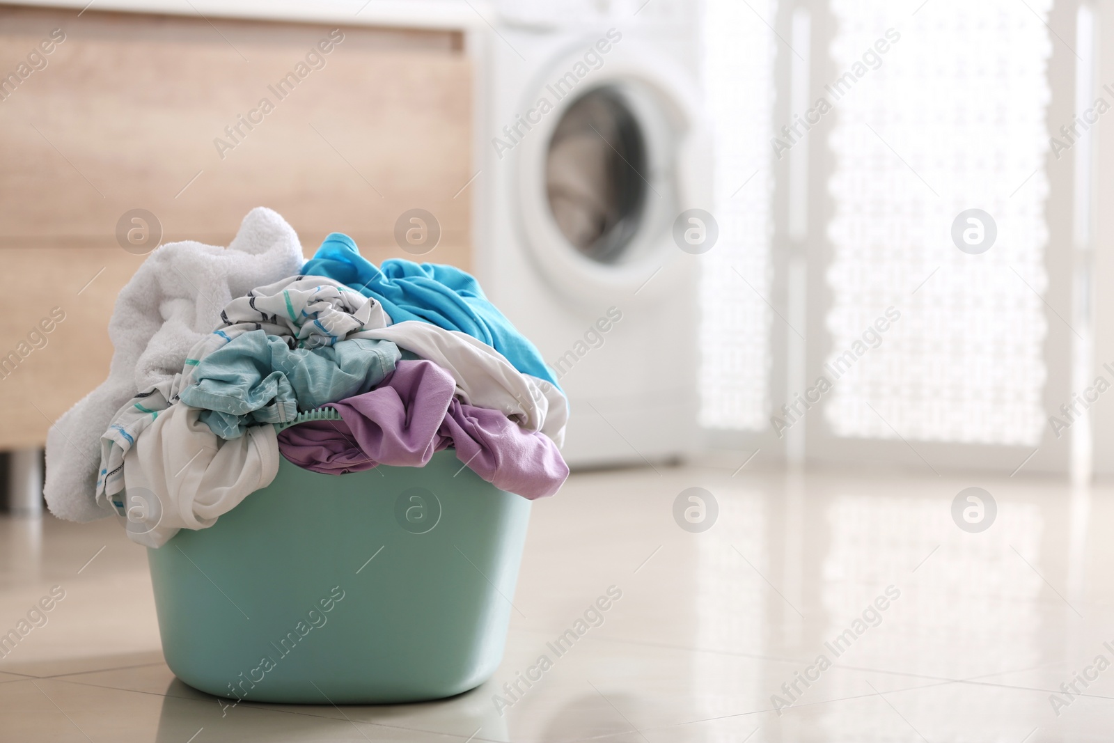 Photo of Plastic basket with dirty clothes on floor in bathroom. Space for text