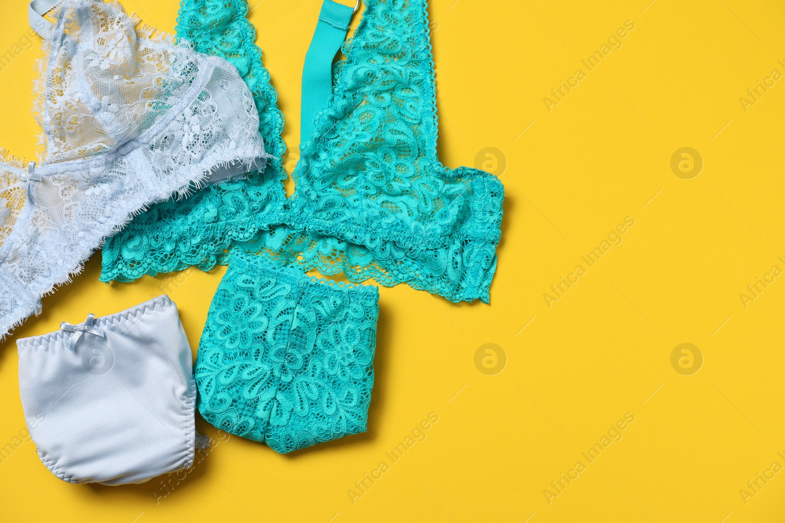 Photo of Stylish folded women's underwear on yellow background, flat lay. Space for text