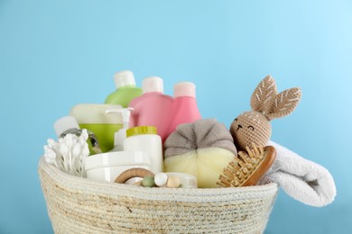 Photo of Basket with baby cosmetic products and accessories on light blue background