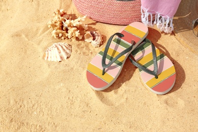 Flip flops and other beach accessories on sand, above view with space for text